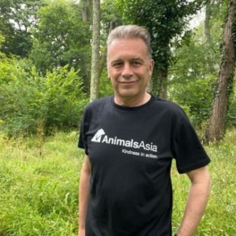 Person in an Animals Asia t-shirt standing outdoors in a green forested area.