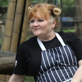 Person wearing bear ear headband, striped apron, and black t-shirt sitting outdoors with bamboo in the background.