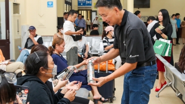 Person distributes reusable bottles to seated people in a busy indoor waiting area, promoting sustainability.