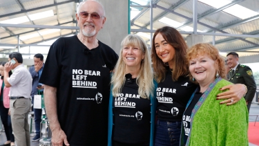 Group of people in "No Bear Left Behind" shirts standing together at an indoor event with others and security personnel in the background.