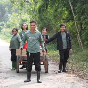 Three women and two men from Vietnam dressed in Animals Asia sweatshirts smile and pose for the camera as they pull a cart through the sanctuary they work in.