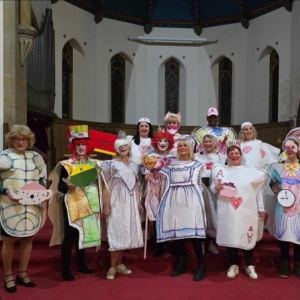 Group wearing colorful hand-drawn costumes posing together inside a church with red carpeting.