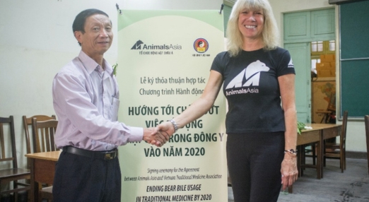 Two people shaking hands in front of an Animals Asia banner at an official partnership event.
