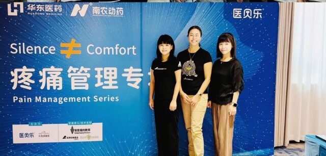 Three women posing in front of large blue banner, printed with English and Chinese words related to animal pain management