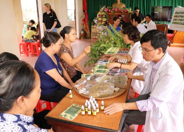 People sitting at a table with staff in white coats and herbal medicine