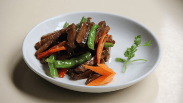 Vegan plant-based meat with red peppers and green beans displayed on a round, white plate.