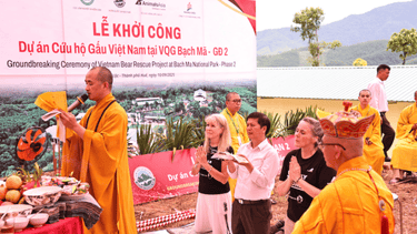 Monks in golden robes blessing a site, with three people kneeling behind them.