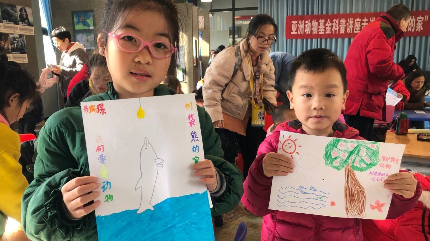 Two Asian school children hold up hand drawn pictures of wildlife