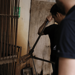 Man in backround using a bolt cutters to break a padlock on a rusted cage.