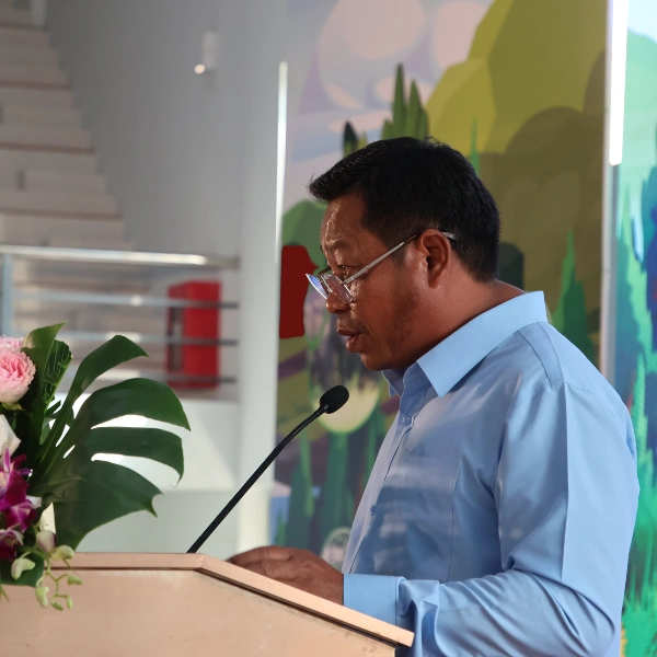 Man in blue shirt, dark hair, glasses speaking at a podium